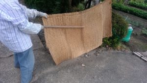 納屋の前で１人でムシロ叩きをする母親